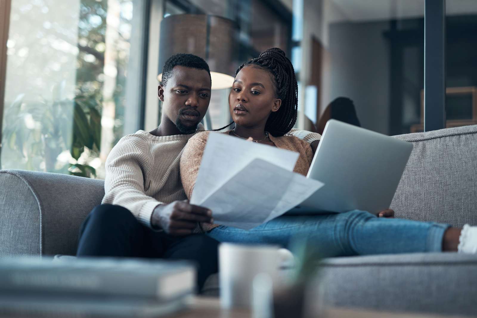 young couple sitting on the sofa together and using a laptop while going through their finances
