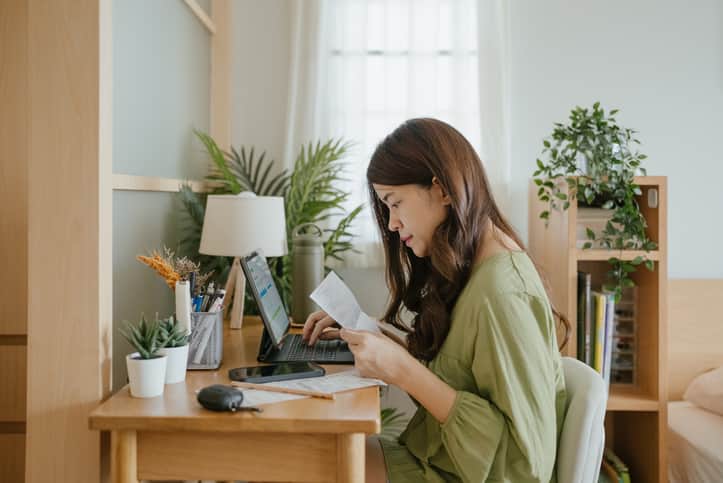 Woman holding paper various expense bills and plans for personal finances at her home